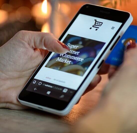Woman using smartphone for online shopping with credit card in hand, festive background lighting.